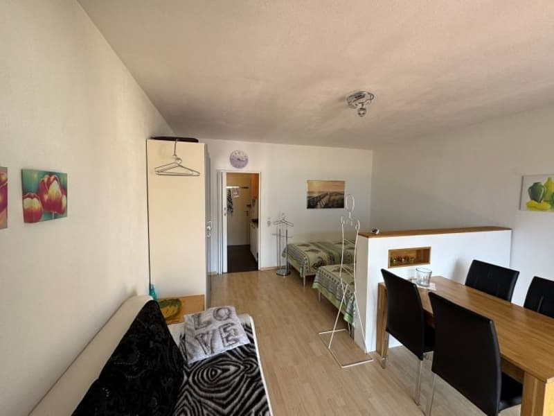 A living room with a couch, a dining table, and a bedroom with two beds.