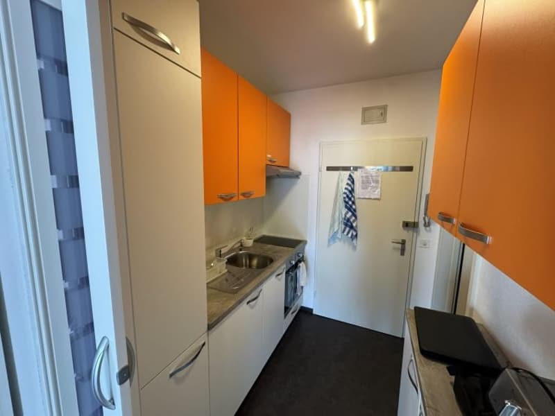 modern kitchen with white cabinets, orange accents, stainless steel sink, dishwasher, washing machine, and a towel hanging on the wall