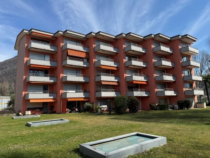 Apartment building, multiple floors, balconies, orange exterior, green lawn, swimming pool
