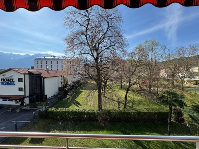 View of a hotel with a garden, trees, and mountains in the background