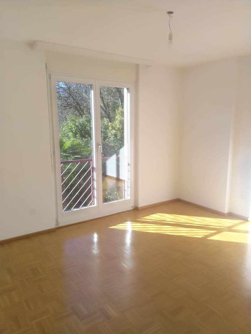 empty room, sliding glass doors leading to balcony, wooden parquet flooring, ceiling light, white walls