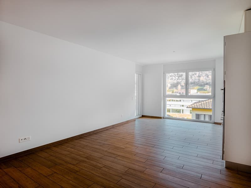 Spacious living room with large windows providing a view, hardwood flooring, and white walls