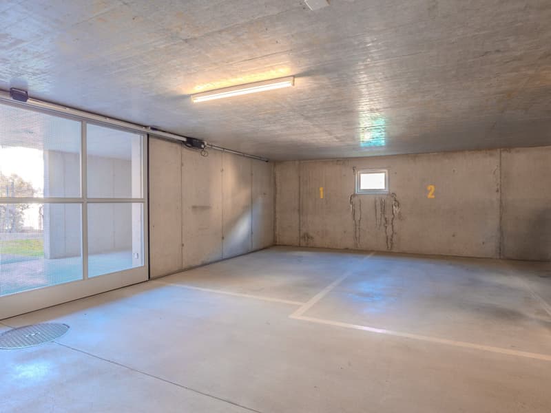 Large open space with concrete floor, fluorescent lighting, and a sliding glass door leading outside.