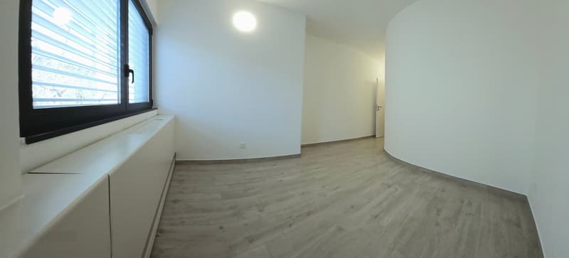 Empty room with white walls and hardwood floors, large window, white cabinets, ceiling lamp