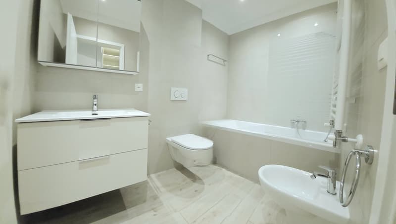Modern bathroom with white fixtures, vanity with drawers, toilet, bathtub with shower, white floor and walls