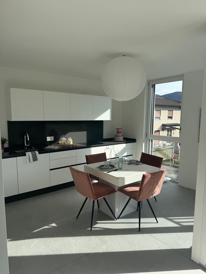 white modern kitchen with dining area, black granite countertops, white cabinets, white flooring, table with four chairs, sink with faucet, window