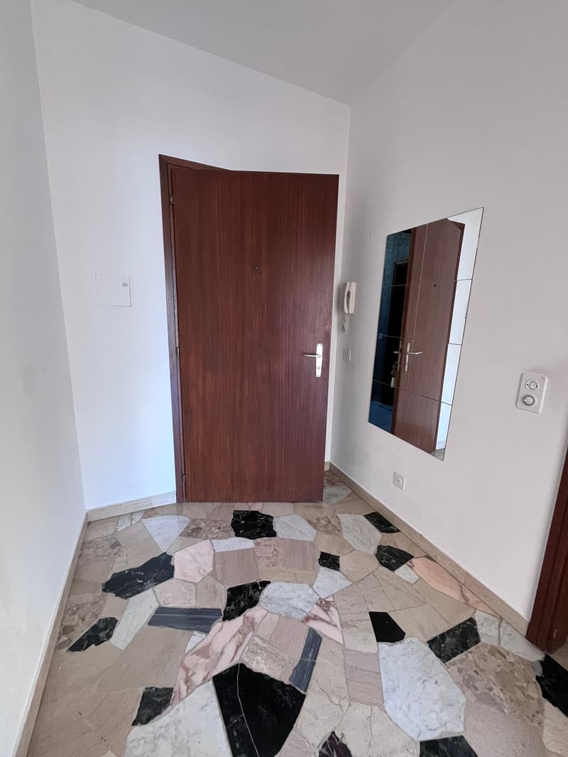 Empty room with white walls, wooden door, mirror, and mosaic floor