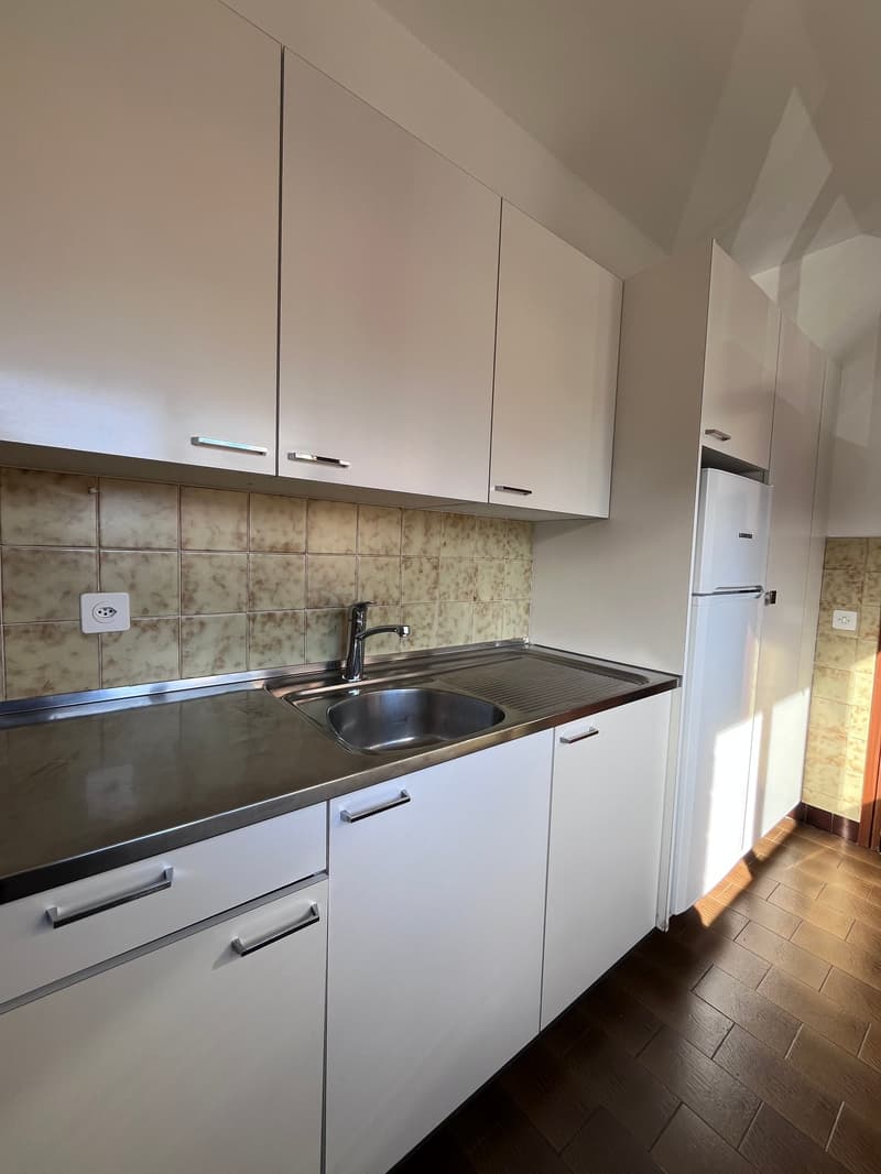 modern kitchen with white cabinets, stainless steel countertop, stainless steel sink, stainless steel faucet, white refrigerator, tiled backsplash, power outlet, wooden floor