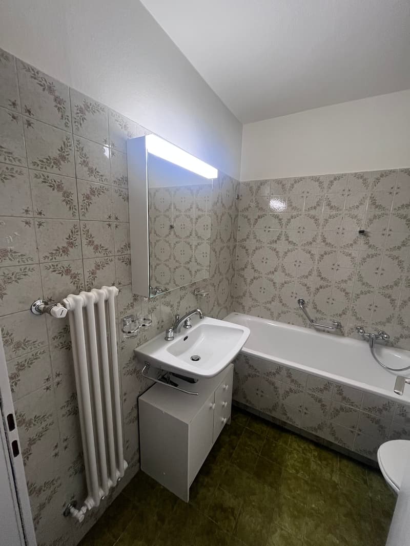 Bathroom with white tiles, white bathtub, white sink, white toilet, white radiator, mirror