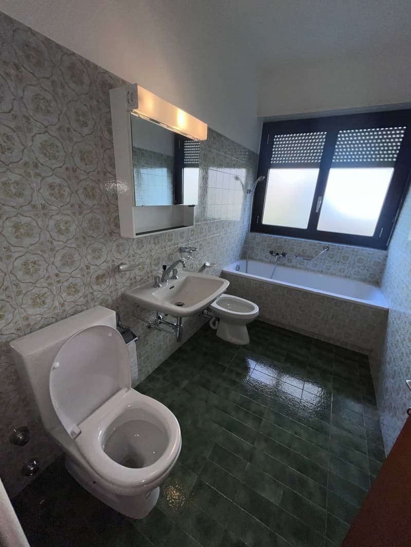 Bathroom with green tiles, white toilet, white sink, white bathtub, mirror, and shower head