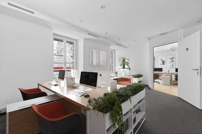 modern office, white walls, wooden desk, red chairs, computer monitors, plants, carpeted floor