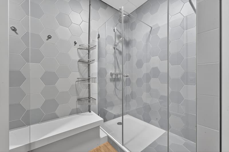 modern bathroom with hexagonal tiles, walk-in shower, small white bench, two metal racks
