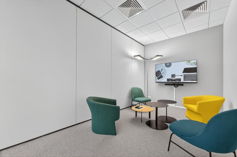 Minimalistic conference room, white walls, carpeted floor, several chairs, tables, TV mounted on the wall