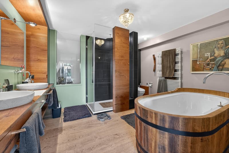 modern bathroom with wooden elements, two sinks, wooden bathtub, glass shower, wooden floor, green wall