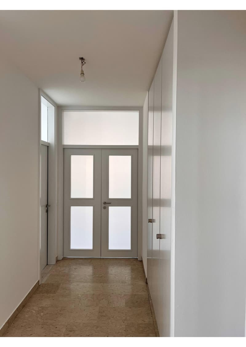 Empty hallway with white walls, double doors, and tiled floor.
