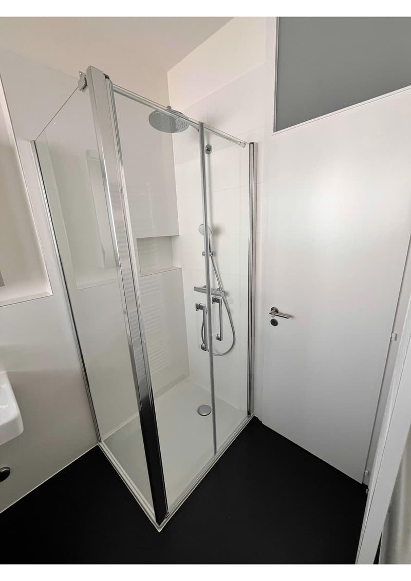 Modern bathroom with glass shower enclosure, white tiles, and a white sink.