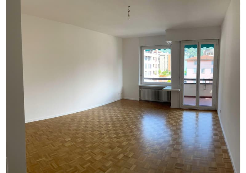 empty room, wooden floor, white walls, sliding glass doors to balcony, radiator, power outlet