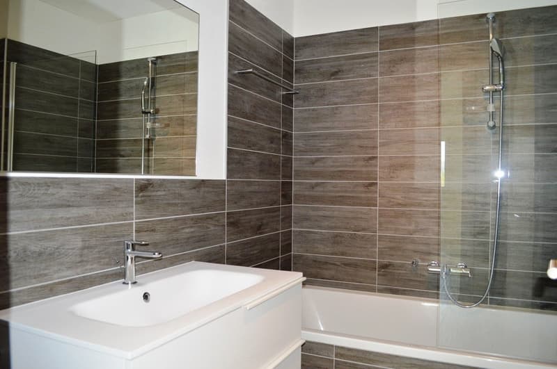 bathroom with tiled walls, white bathtub, white sink, silver shower head, and a mirror