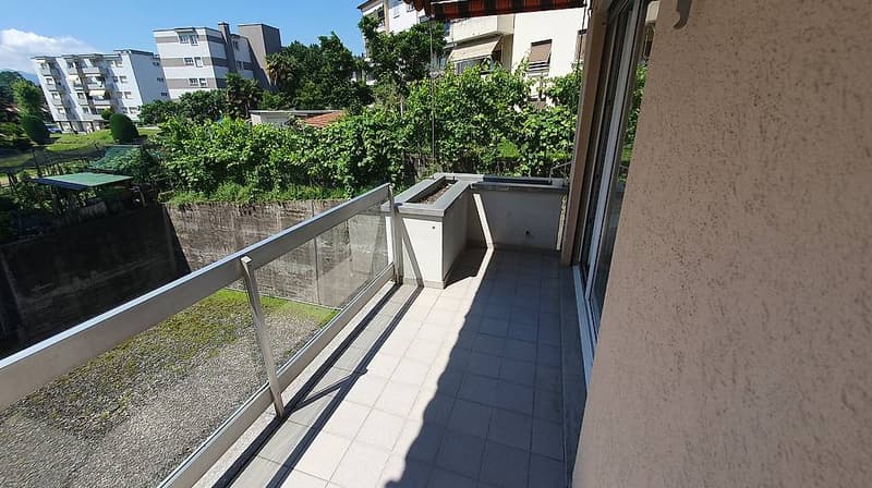 Balcony with glass railing, tiled floor, view of greenery and buildings