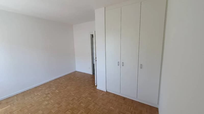 Spacious bedroom with white walls, hardwood flooring, and built-in closet units along the wall.