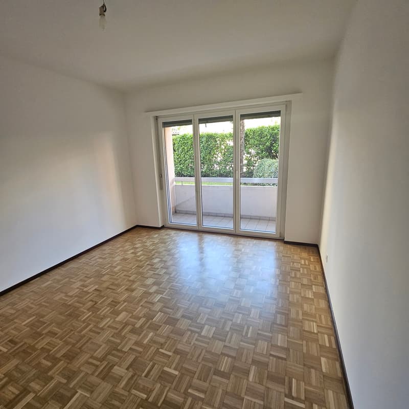 Spacious room with large windows overlooking a balcony or terrace, hardwood parquet flooring, and white walls.