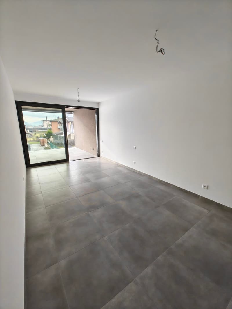 Large empty room, gray tiles, sliding glass door leading to balcony, white walls