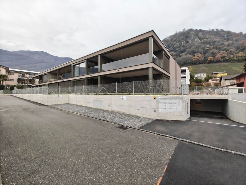 Modern building with glass walls, concrete driveway, underground parking, large balconies, fenced entrance