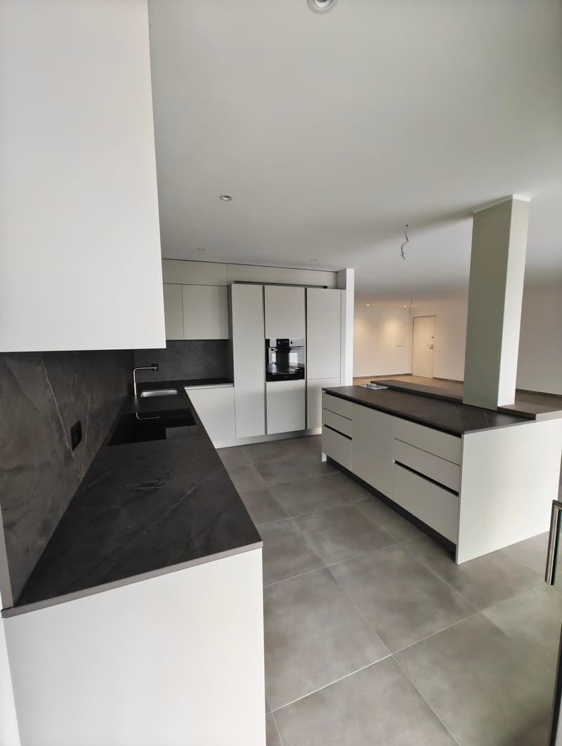 modern kitchen with white cabinets, black countertops, gray tiled floor, stainless steel faucet, integrated oven and dishwasher