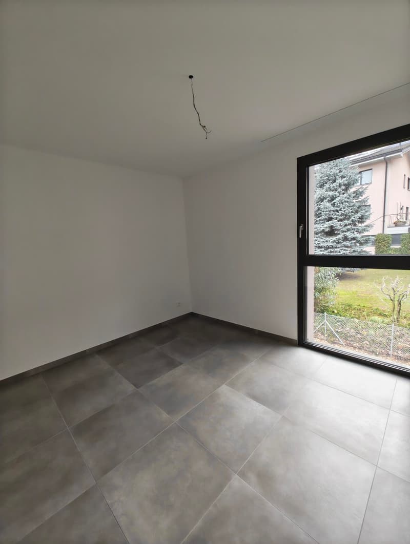 Empty room, white walls, gray floor, sliding window, outside view of a garden