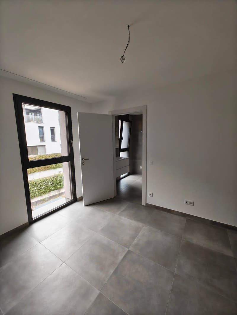 open space room with a door leading to the inside, with tiled flooring, large windows, and a small hedge outside
