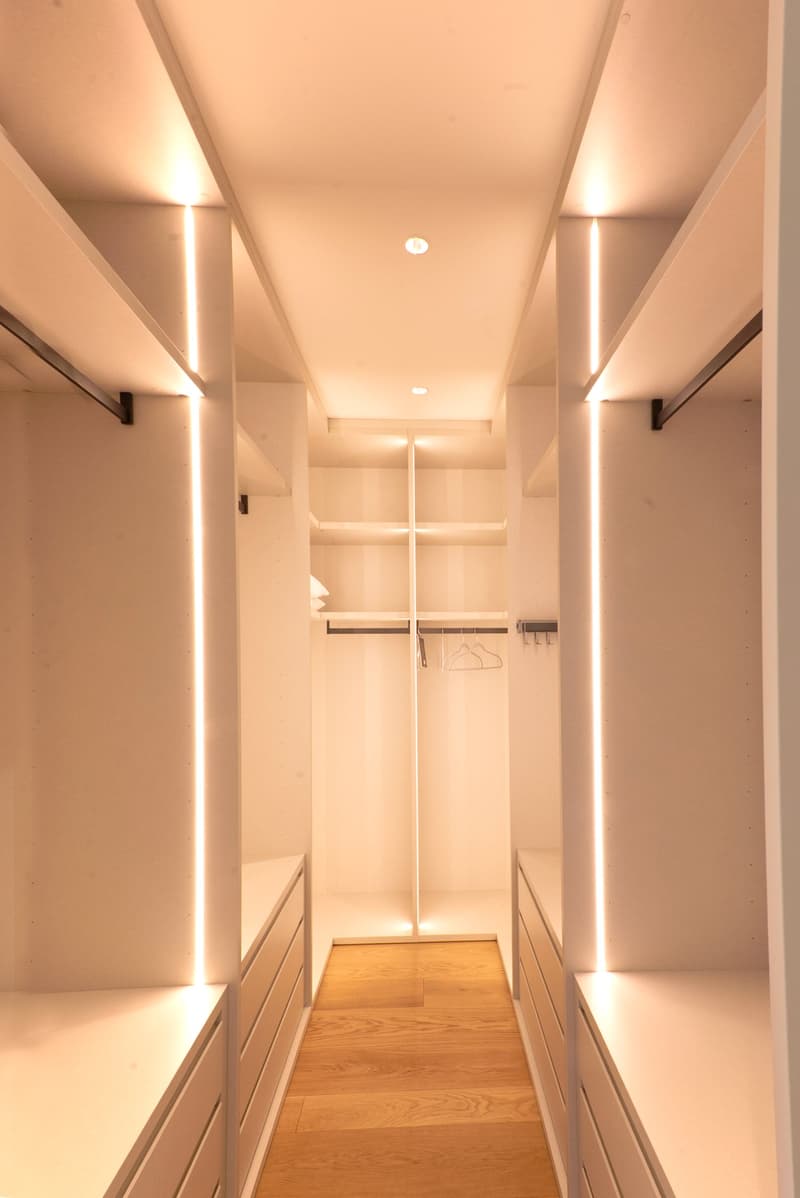 Spacious walk-in closet with built-in shelves and hanging rods, hardwood flooring, and recessed lighting along the walls.