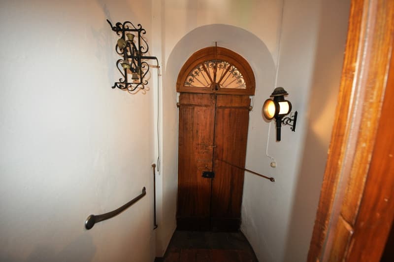 Wooden arched doorway, ornate metal light fixture, wooden door with decorative design, stone walls