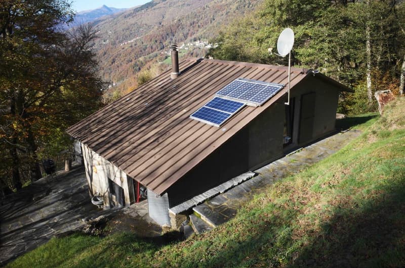 Mountain house with raised ground floor, solar panels on roof, surrounded by trees and grass