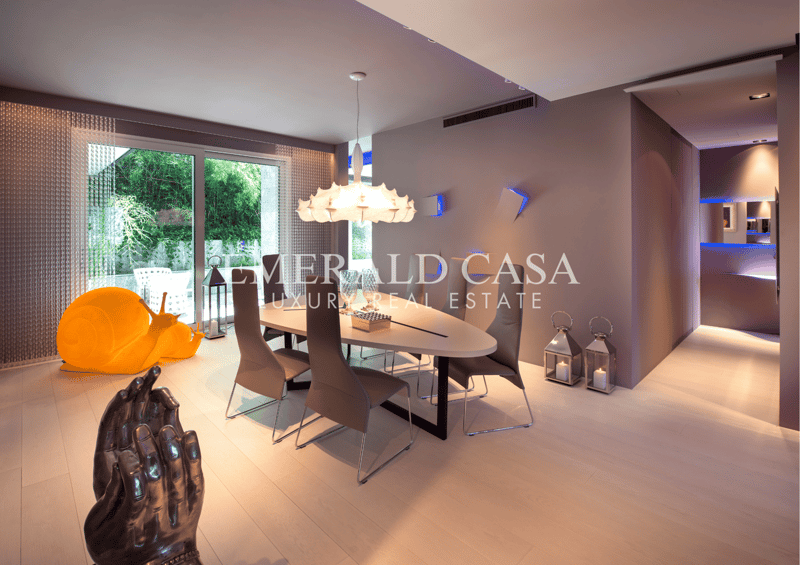 Spacious dining area with large windows overlooking a garden, modern dining table and chairs, pendant lighting fixture, and decorative accents.