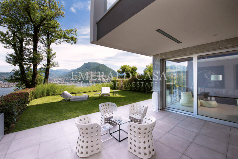 Modern house with large windows, balcony, and outdoor seating area overlooking a scenic mountain landscape