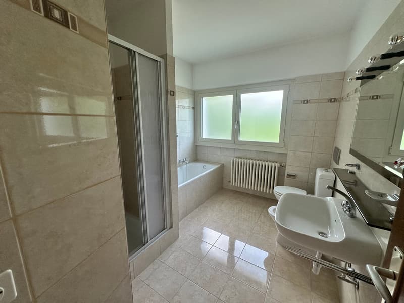 Spacious bathroom with tiled walls and floor, a bathtub, a sink, and a window providing natural light.