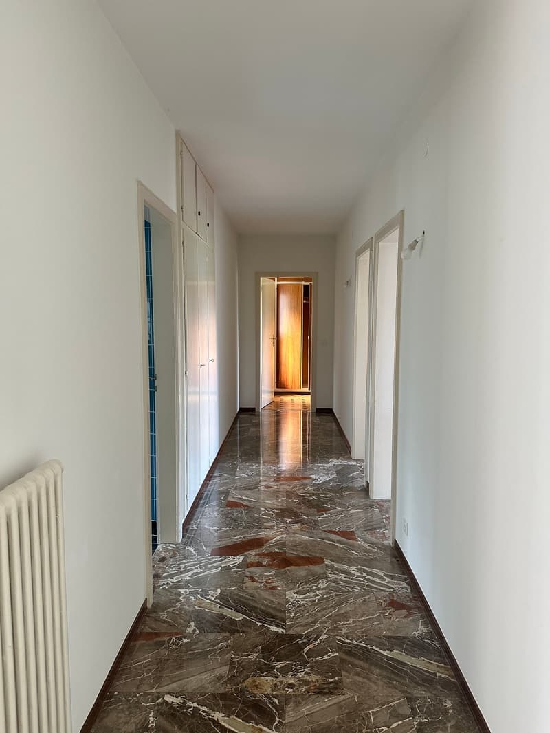 Long hallway with white walls, marble-patterned tile flooring, and built-in closets or cabinets along the walls.