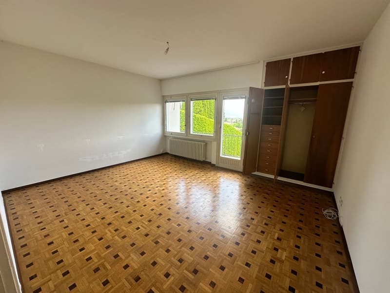Spacious bedroom with large windows, hardwood parquet flooring, and built-in wooden wardrobes.