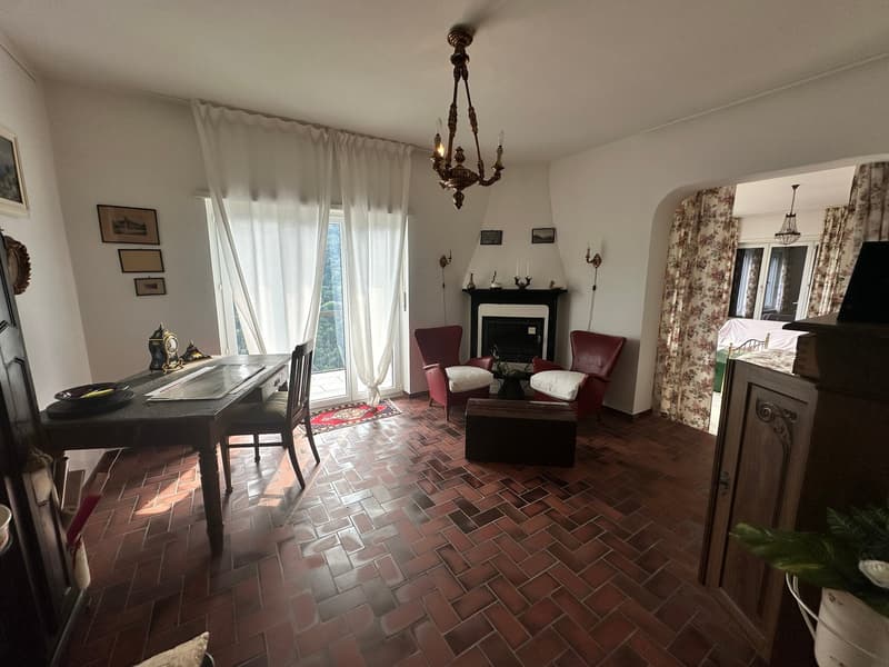 red tile floor, chandelier, fireplace, dining table, 2 red armchairs, windows with curtains, decorative items