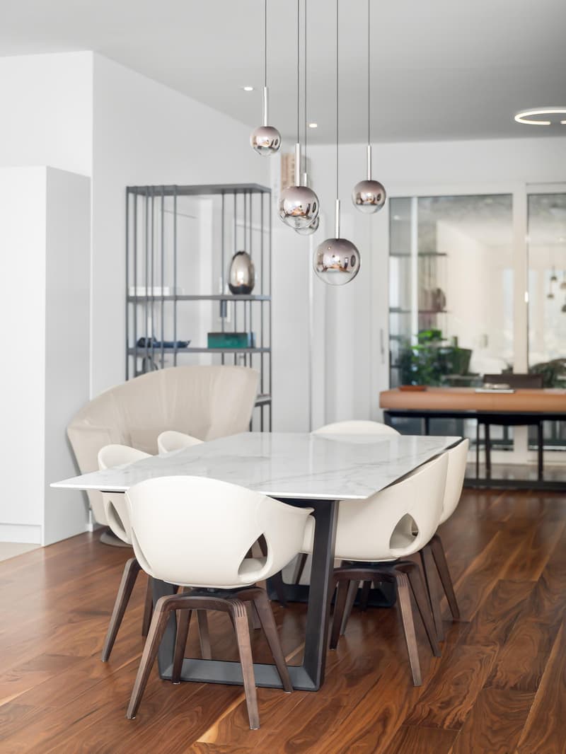 marble dining table, white modern chairs, chrome light fixtures, white walls, wooden floor, armchair, shelves