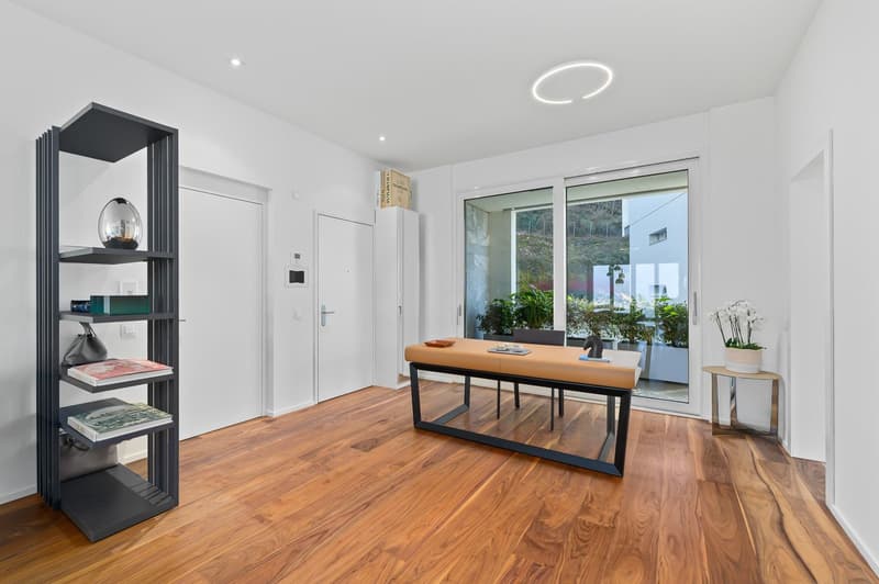 wooden floor, white walls, modern desk with leather top, metal shelving unit, open sliding glass door to a balcony with plants