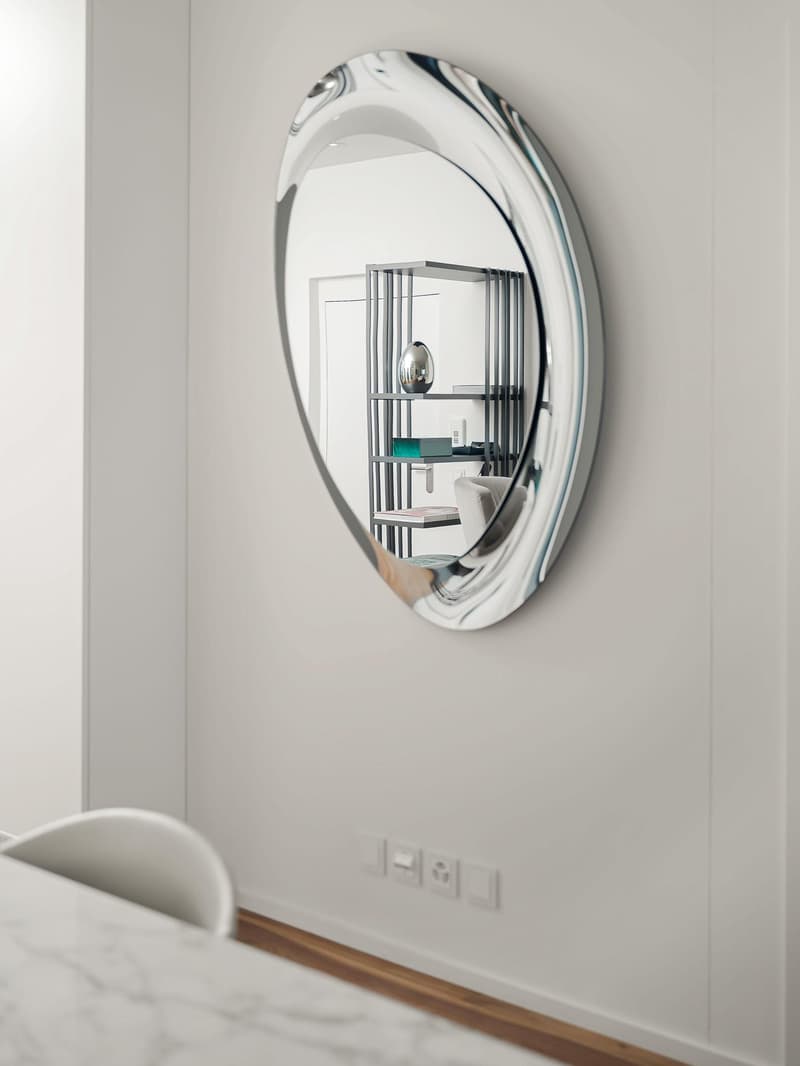 Room with white wall and floor, white table and chair, large round mirror on wall