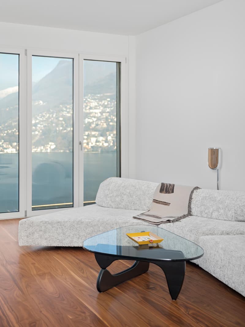 Modern design, light wooden floor, large windows, large L-shaped sofa, glass coffee table, artwork, scenic view