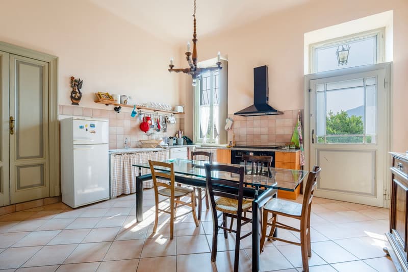 glass table, wooden chairs, refrigerator, cabinets, chandelier, white tile floor, double door entrance, wooden door, large window, exhaust hood, stove, sink