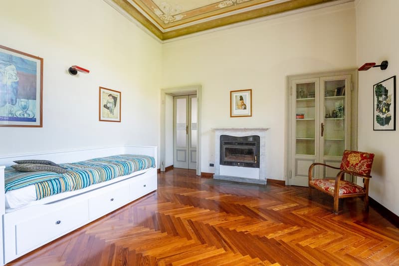 wooden floor, a bed with drawers, a fireplace, a chair, picture frames, a white cupboard, lamps