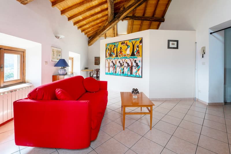 Living room with wooden beams ceiling, red sofa, wooden coffee table, paintings on the wall, lamp