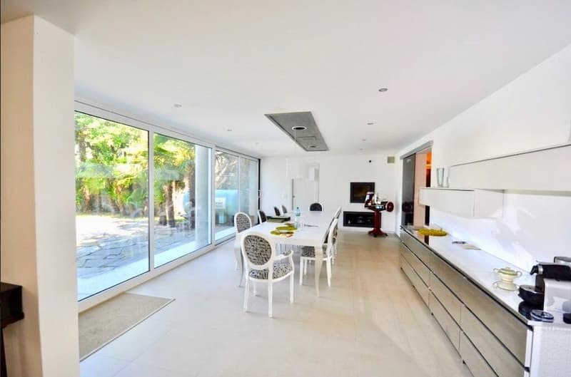 modern white kitchen with glass sliding door, dining table, island countertop, large windows, coffee maker, dishwasher