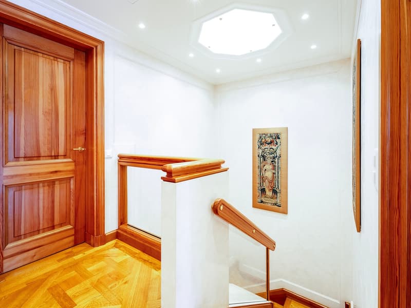 White walls, wooden floor, double doors, staircase with wooden handrail, small light fixture, picture on wall