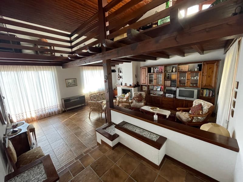 Living area with wooden beams, wooden shelves, living room set with sofa, fireplace, television, wooden chairs, tables, curtains
