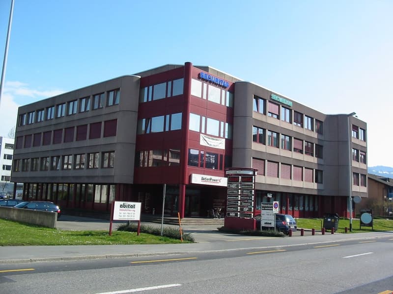 Office building, red facade, multiple windows, multiple floors, signboard, cars parked in front